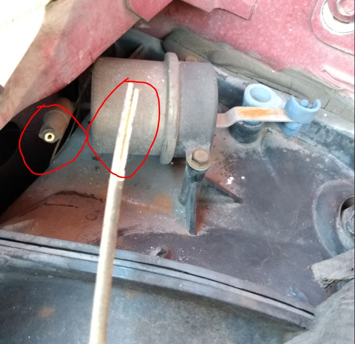 Close-up of a vehicle's engine bay showing a part circled in red, with a metal rod extending downwards