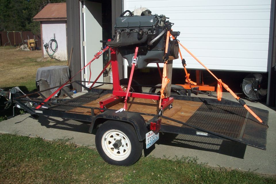 Engine on red stand secured with straps on a utility trailer with a license plate
