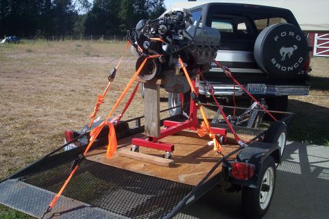 1978 Ford Bronco - A 1978 Ford Bronco is parked behind a trailer carrying an engine, secured with orange straps.