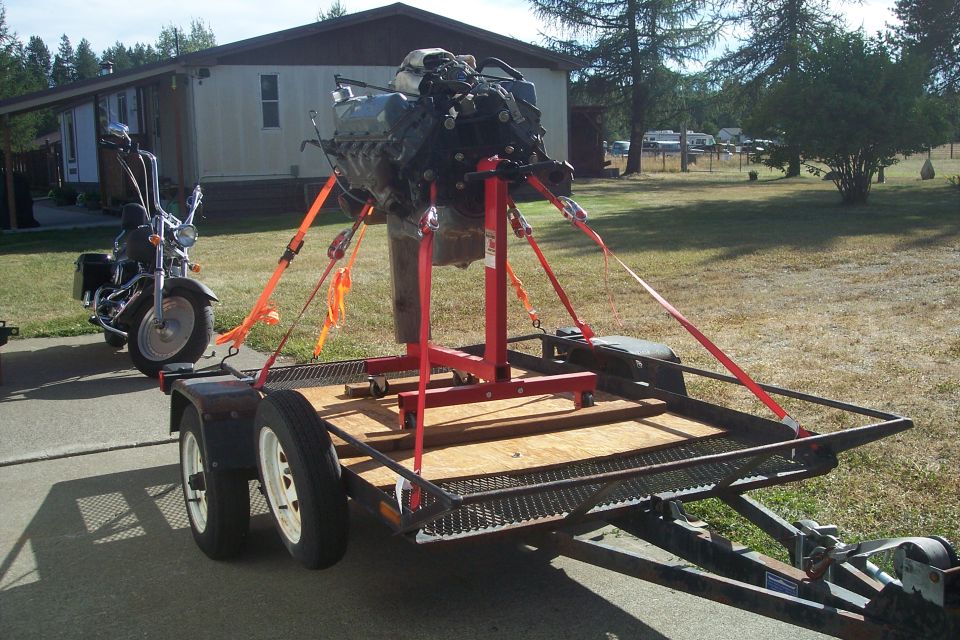 Engine on red stand secured to trailer, motorcycle parked nearby
