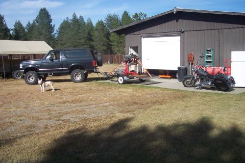 1978 Ford Bronco - A black Ford Bronco is parked outside a garage, towing a trailer, with a motorcycle nearby.