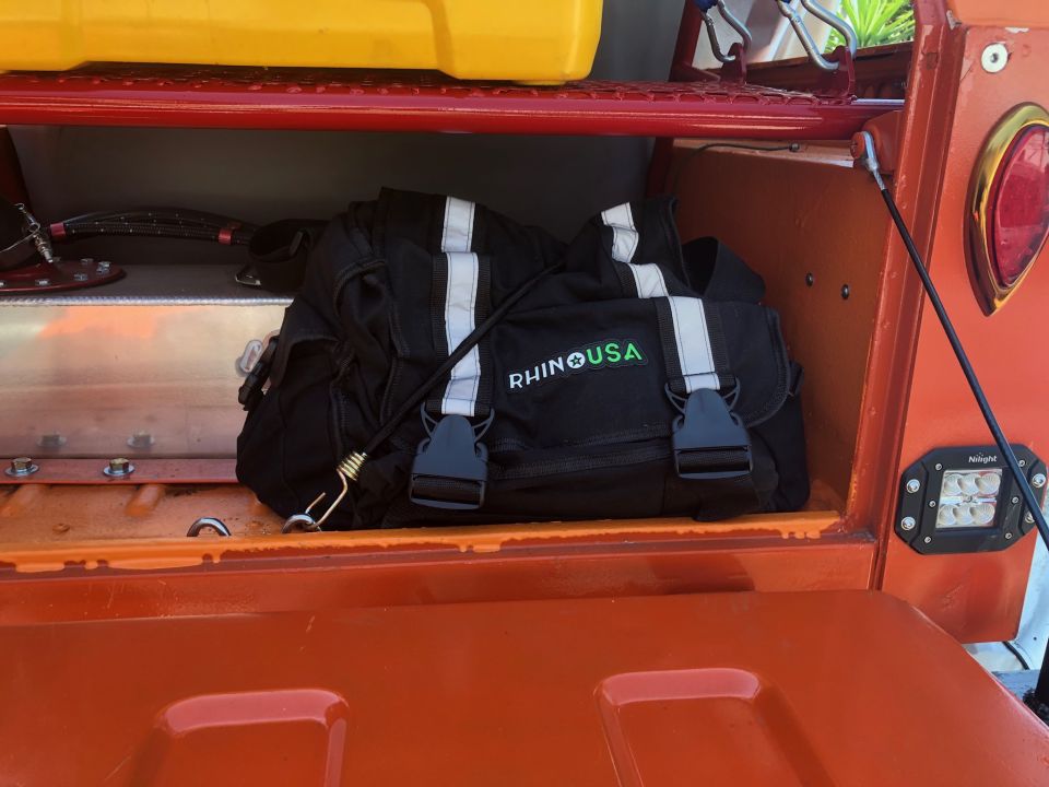 Orange vehicle bed storage with black bag that says RHINO USA. Also a yellow container on top shelf