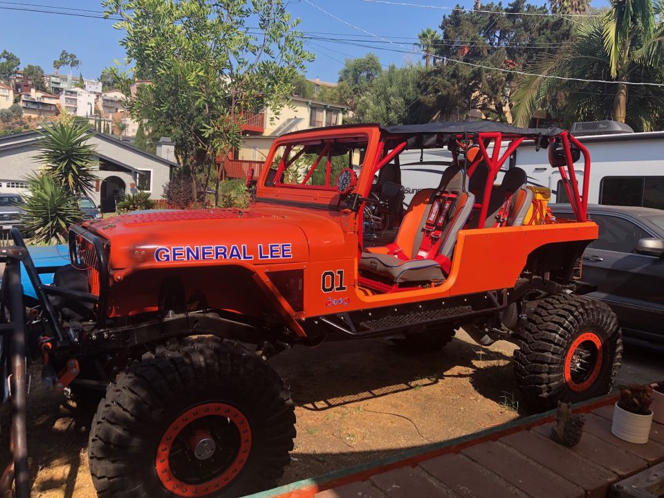 Orange Jeep Wrangler with "GENERAL LEE" and "01" graphics, roll cage, and racing seats