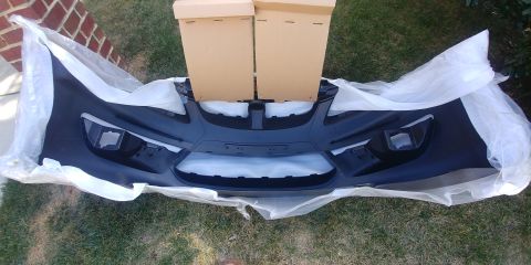 1996 Ford Bronco - A new front bumper is shown, packaged for shipping, resting on grass.