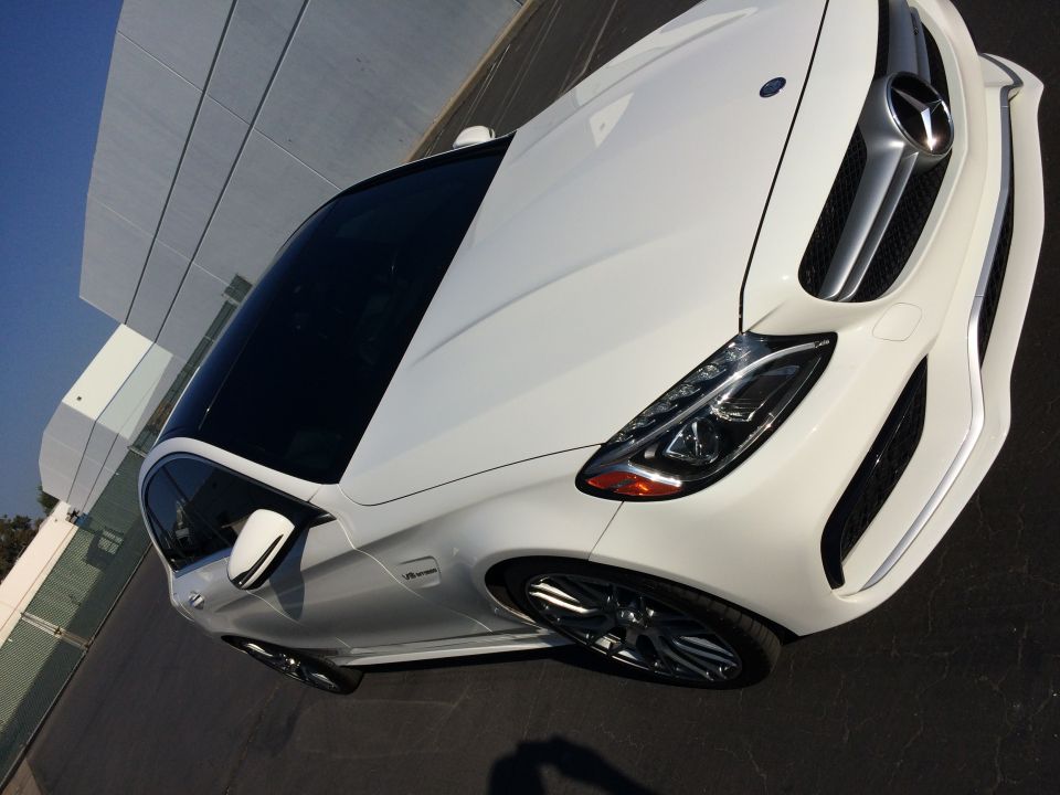 White Mercedes-Benz sedan parked in front of a modern building. The car has a black roof and tinted windows