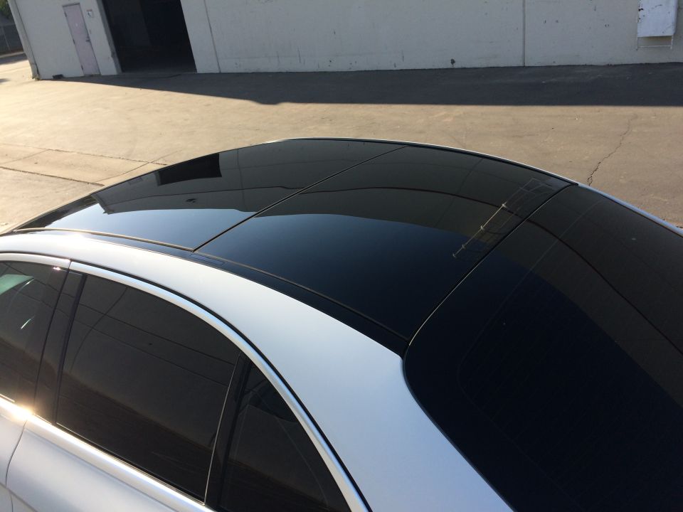 Top view of a white car with a black panoramic sunroof. A building is in the background