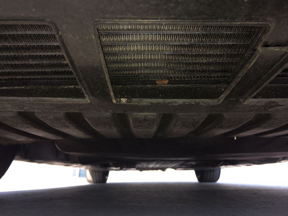 Underside of a vehicle showing two radiators and undercarriage panels. Tires visible