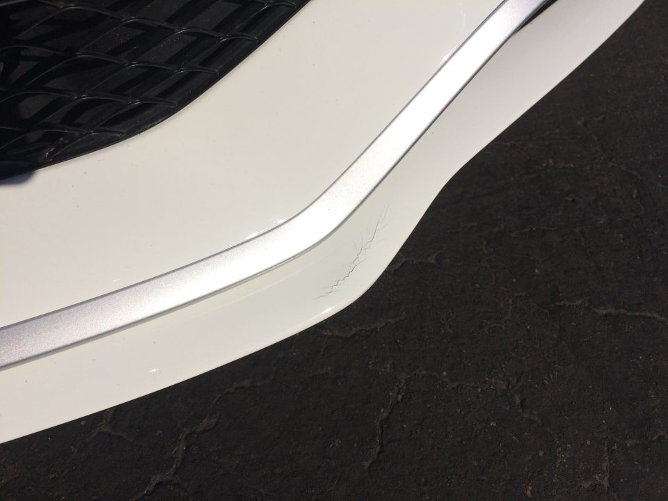 Close-up of a white car bumper showing a chrome trim piece with visible cracks underneath