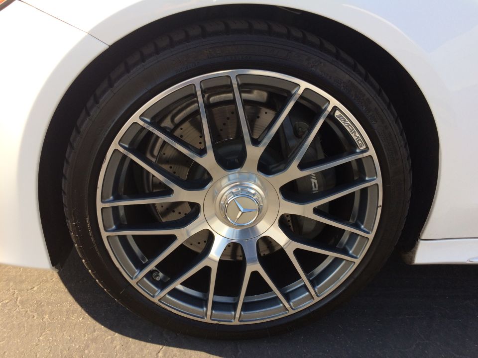 Close-up of a Mercedes-Benz wheel with an AMG logo on one of the spokes. Perforated brake rotor visible behind the wheel