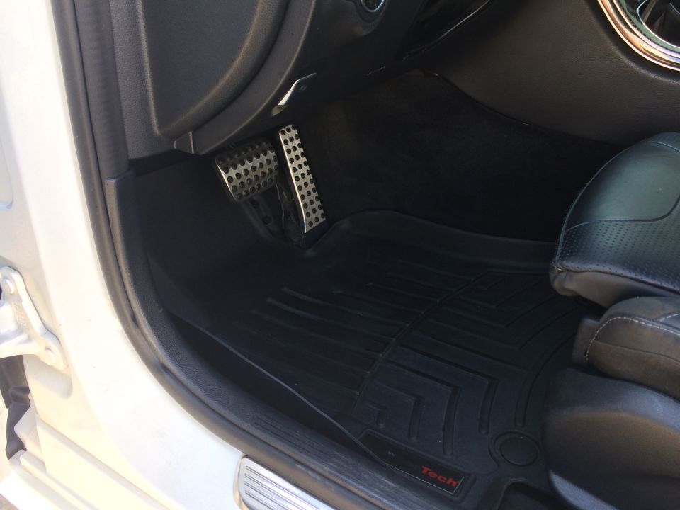 Car interior showing black floor mats and metal pedals