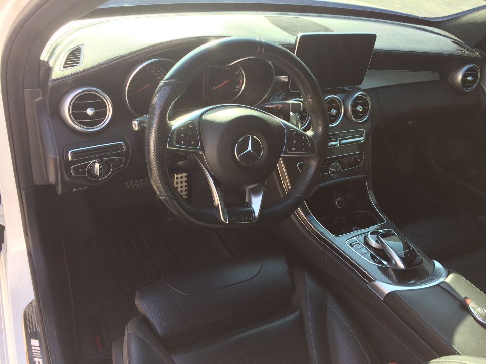 Black leather interior of a Mercedes-Benz C-Class, showing the steering wheel, dashboard, and center console