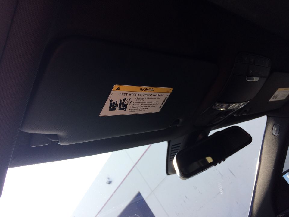 Interior view of a car's sun visor with a warning label, rearview mirror, and overhead console