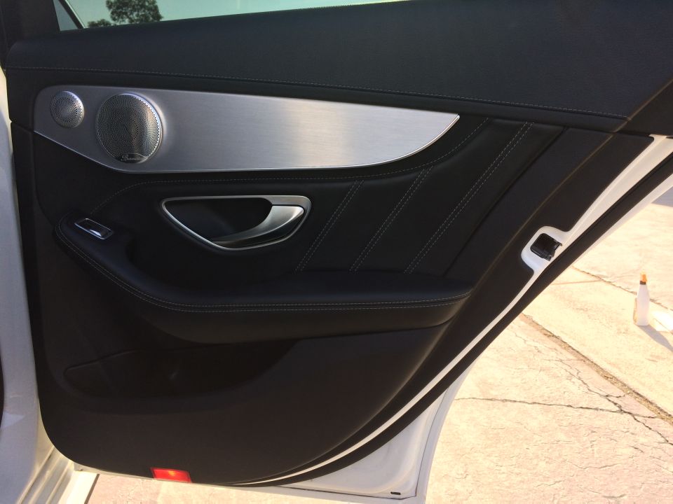 Black leather car door interior with brushed metal trim and speaker grille