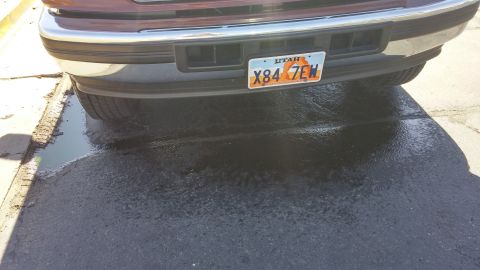 1996 Ford Bronco - A vehicle's rear bumper and license plate are visible, with a puddle on the ground beneath it.