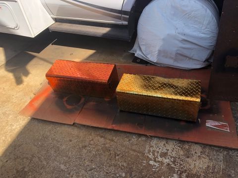 1992 Jeep Wrangler - Two diamond plate toolboxes, one orange and one gold, are drying on a cardboard mat after being spray painted.