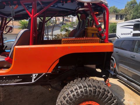 1992 Jeep Wrangler - This heavily modified off-road vehicle features a bright orange body, a custom roll cage, and large, aggressive tires.