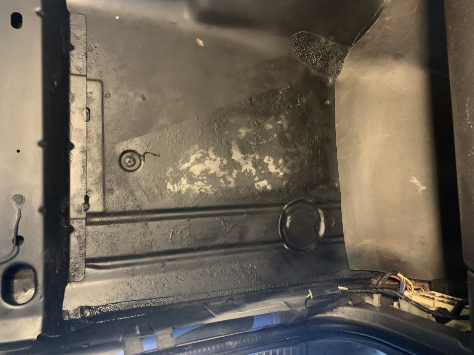 Interior view of a vehicle's cargo area, showing black painted metal with some white residue and wiring harness