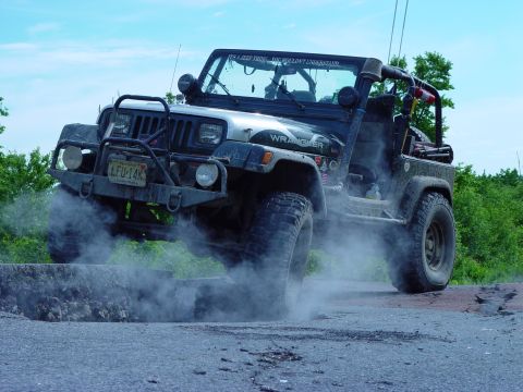1992 Jeep Wrangler - This Jeep Wrangler is navigating a challenging off-road terrain, creating a cloud of dust.