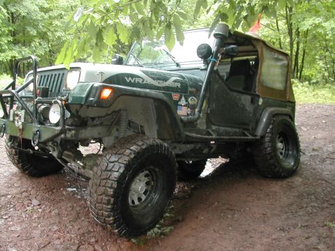 1992 Jeep Wrangler - A modified 1992 Jeep Wrangler sits on a muddy trail surrounded by trees.