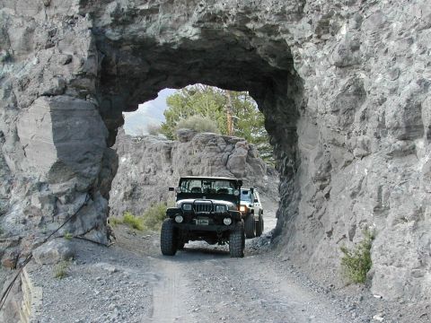 1992 Jeep Wrangler - Two Jeep Wranglers navigate a narrow dirt path through a natural rock archway.