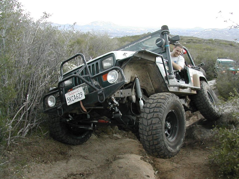 White 1992 Jeep Wrangler with aftermarket bumper and snorkel on a rocky trail