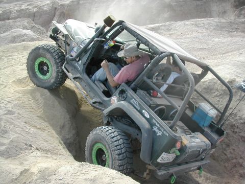 1992 Jeep Wrangler - Modified Jeep Wrangler tackling an off-road obstacle with a driver and passenger inside.