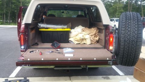 1996 Ford Bronco - The open rear cargo area of a maroon 1996 Ford Bronco reveals tools, a storage bin, and a spare tire mounted externally.