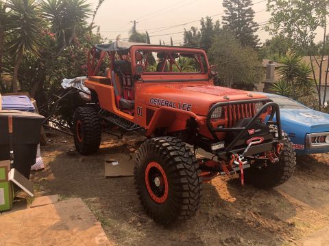 1992 Jeep Wrangler - This modified Jeep Wrangler, labeled "GENERAL LEE", is parked outdoors next to a blue car.