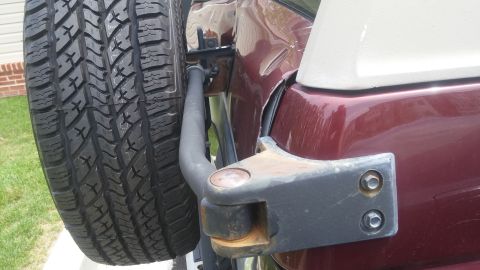 1996 Ford Bronco - A close-up of a maroon SUV's rear quarter panel shows a spare tire carrier and signs of wear and tear.
