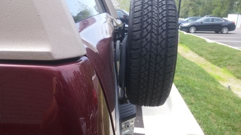 1996 Ford Bronco - Rear view of a red SUV showing a mounted spare tire, with other vehicles visible in the background parking lot.