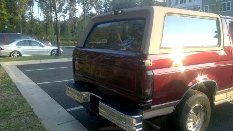 1996 Ford Bronco - Rear view of a maroon Ford Bronco with a tan removable top, parked in a lot.