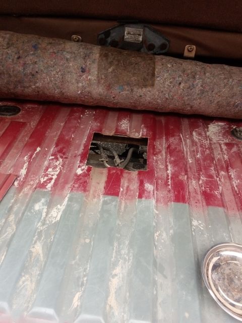 1994 Ford Bronco - Underneath the cargo area floor, hoses and wiring are visible through a cut-out opening.
