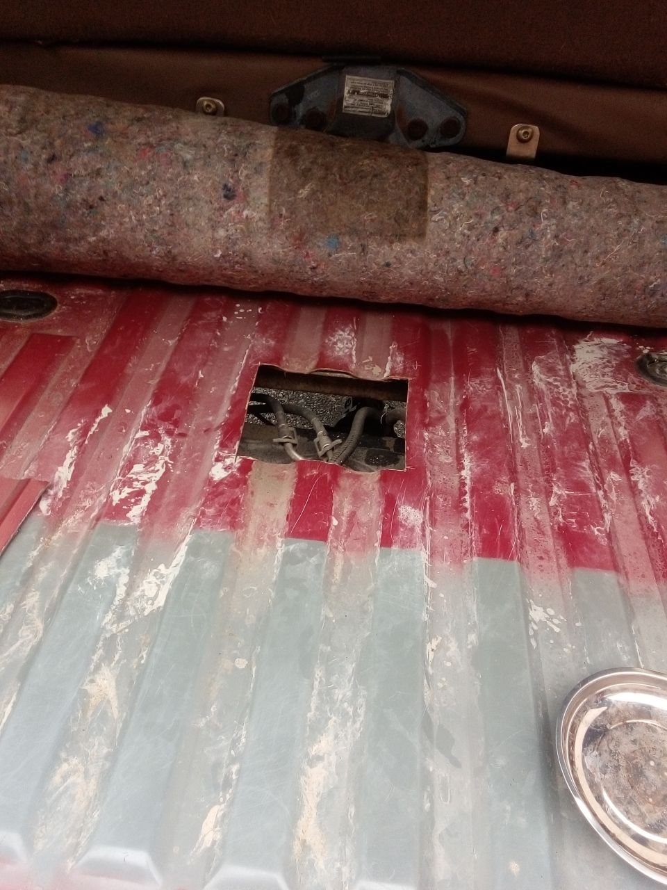 View of the cargo area floor with a cut-out revealing hoses and wiring
