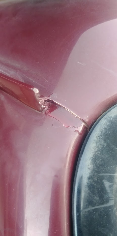 1996 Ford Bronco - Damage to a red car's body panel is visible, with cracked paint and a dark circular object nearby.