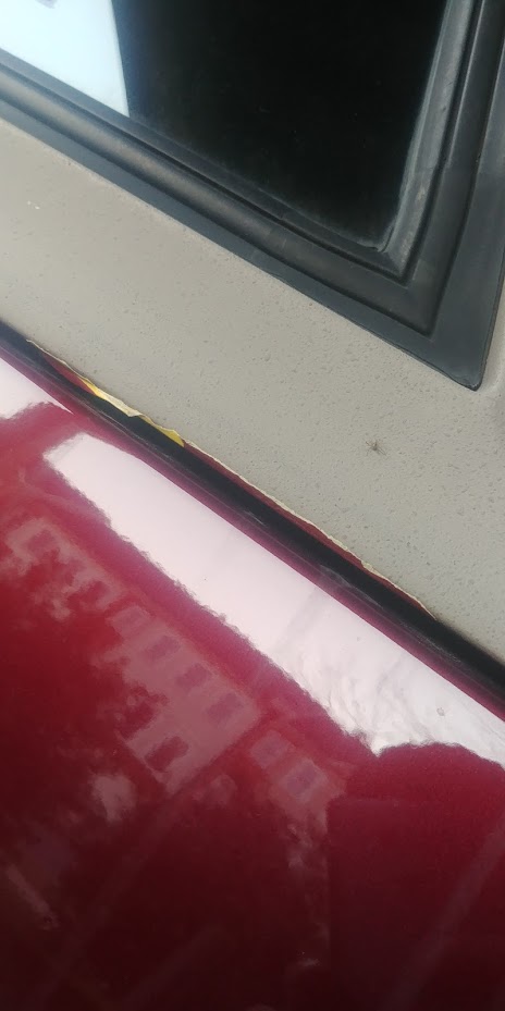 1996 Ford Bronco - Close-up of rust forming on the edge of a red car door, adjacent to a black seal.