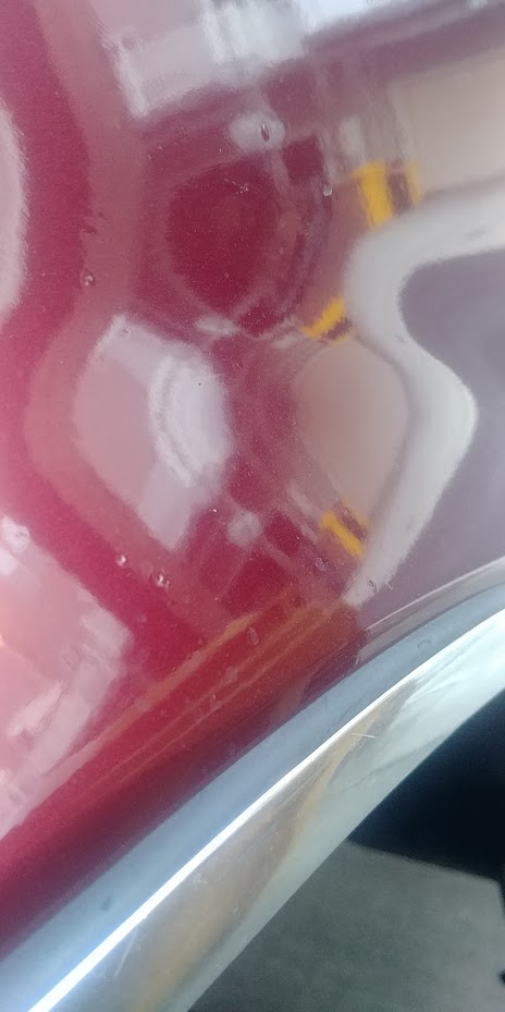 1996 Ford Bronco - Close-up of a red vehicle's body panel with chrome trim, showing water droplets on the surface.