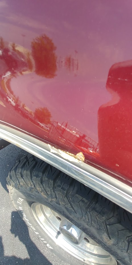 1996 Ford Bronco - Close-up of a 1996 Ford Bronco's red side panel, revealing rust damage and a tire tread.