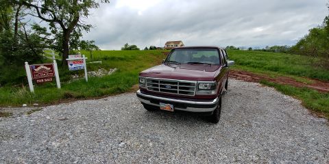 1996 Ford Bronco - This maroon 1996 Ford Bronco is parked on a gravel lot near 'For Sale' signs, under a cloudy sky.