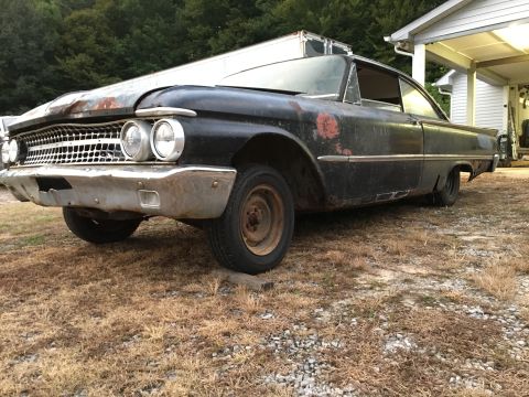 1961 Ford Starliner - This black Ford sedan shows significant wear and tear, with rust visible on the body and a damaged front bumper.