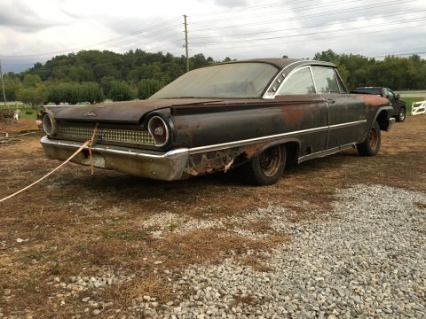 1961 Ford Starliner - A heavily rusted 1960 Ford coupe sits outdoors, with a second vehicle visible in the background.