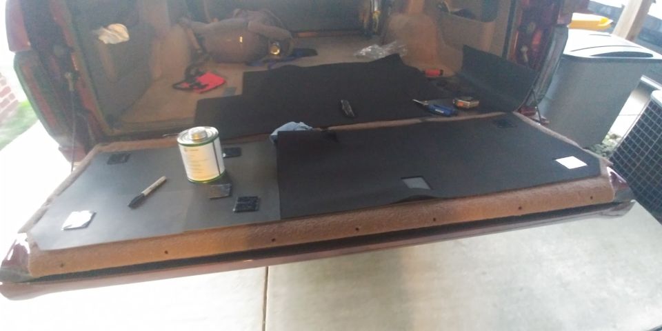 Maroon SUV interior rear cargo area with black carpet pieces and adhesive can on the tailgate