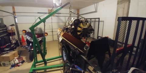 1996 Ford Bronco - A large engine is suspended by a green engine hoist in a garage, with a motorcycle visible in the background.