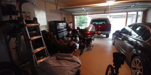 1996 Ford Bronco - A red pickup truck is parked in a garage, seen from the rear, alongside a motorcycle and a dark sedan.