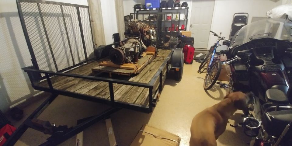Trailer loaded with engine parts, parked next to motorcycles and a bicycle in a garage