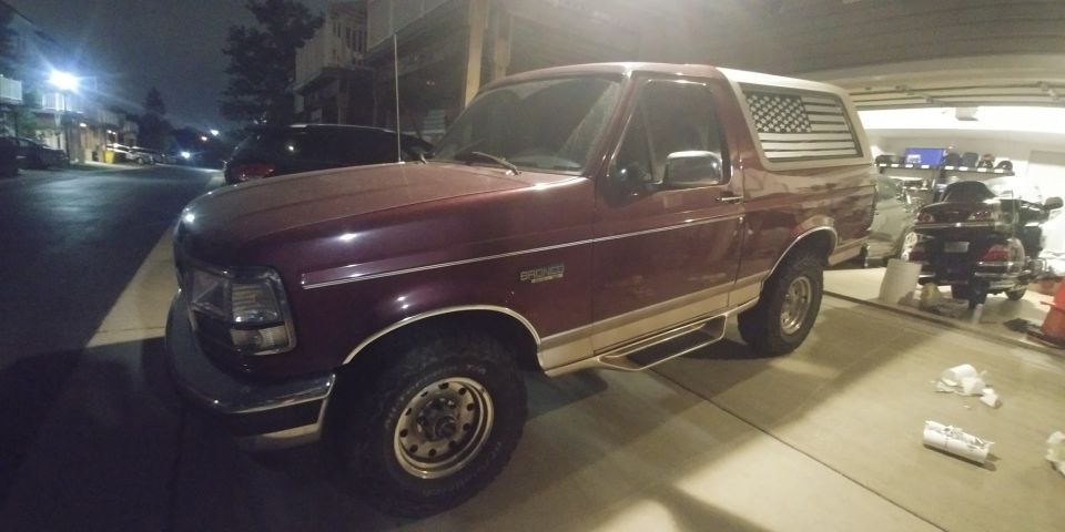 Maroon Ford Bronco with American flag decal on rear window, parked in garage