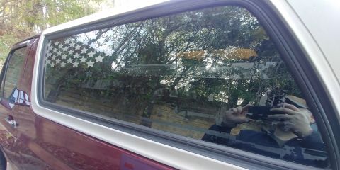 1996 Ford Bronco - A maroon Ford Bronco with a white roof trim is seen from the side, reflecting trees and a person taking the photo.