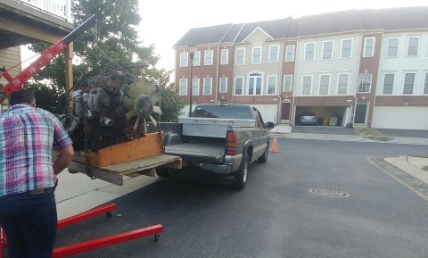 1996 Ford Bronco - An engine is being loaded into the bed of a pickup truck using an engine hoist, with townhouses in the background.