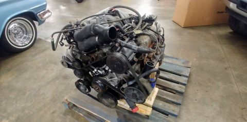 1996 Ford Bronco - Engine removed from a vehicle, sitting on a wooden pallet. A portion of a blue car is visible on the left.