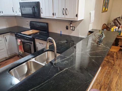 1980 Yugo Vega - A kitchen remodel features dark granite countertops with prominent white veining, a double basin sink, and a stainless steel gas range.