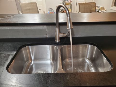 1980 Yugo Vega - A modern kitchen sink with a pull-down faucet is shown with water running. The countertop appears to be granite or a similar stone material.